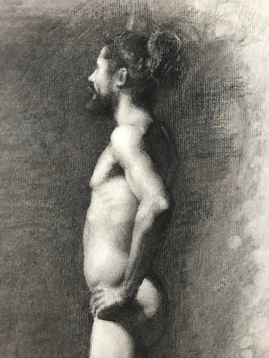 A black and white charcoal drawing of a nude male figure in profile. The man stands with hands on hips, hair in a bun, and a beard. The background is textured, adding depth to the artwork.