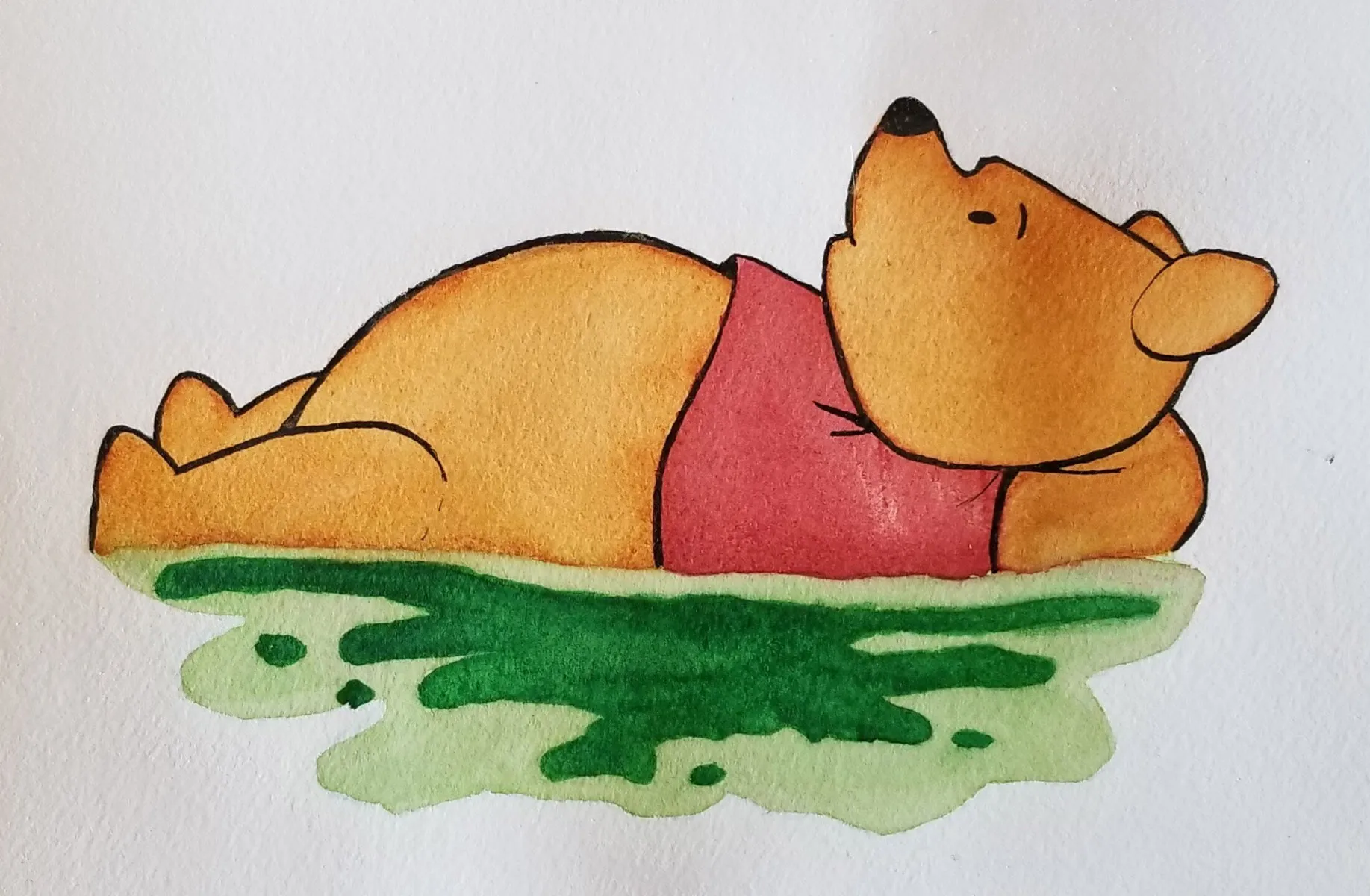 A cartoon brown bear wearing a red shirt lies on its back, relaxing on a green grassy surface. The bear appears content, with its paws behind its head and eyes closed.
