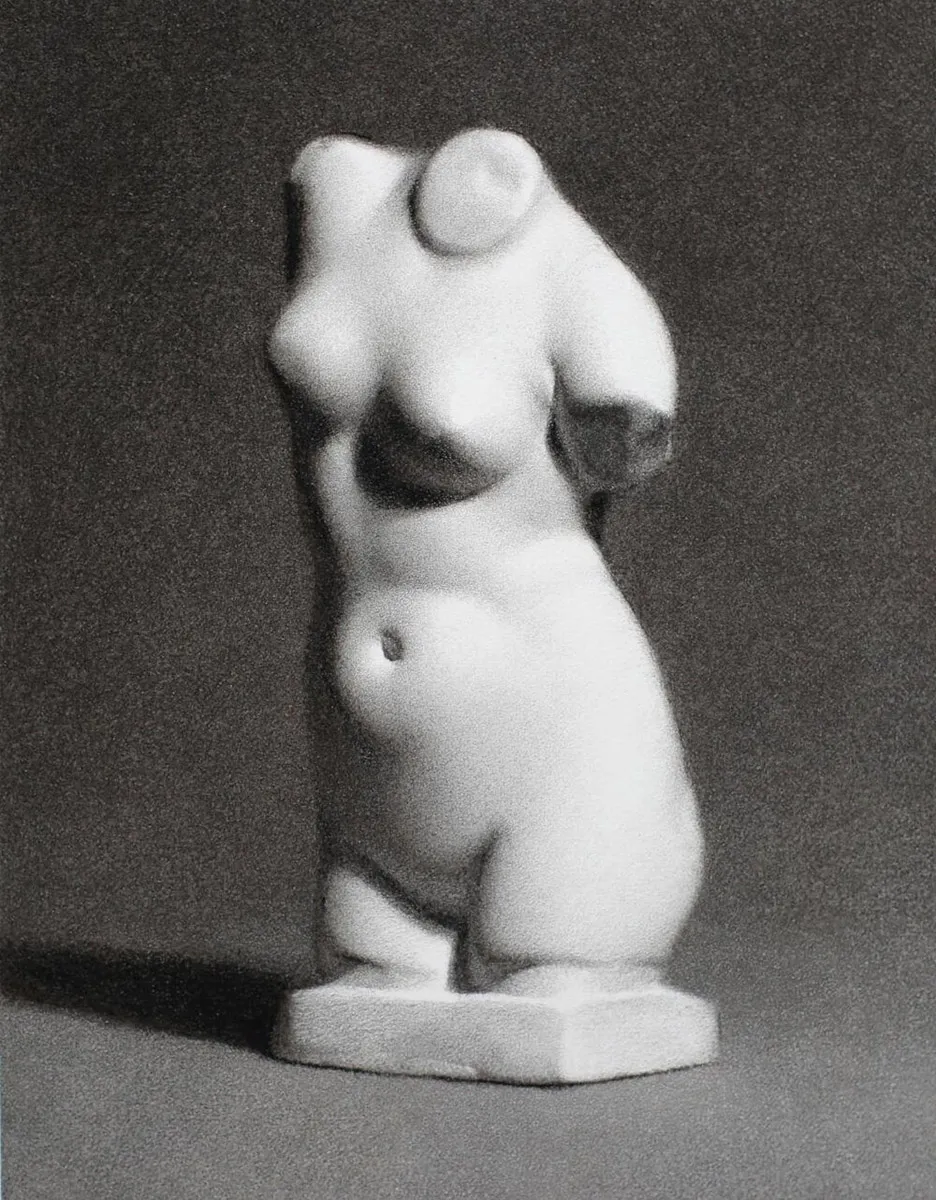 A grayscale image of a white, abstract female torso sculpture without arms or a head. The sculpture stands on a small rectangular base against a plain gray background. Shadows emphasize the smooth, rounded contours of the figure.